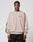 A man wears the LIVE FAST DIE YOUNG Live For It Sweater—a loose, beige 100% cotton sweatshirt with LIVE IT FAST on the chest and black sleeve text—in an oversize fit, standing against a plain background with a neutral expression.