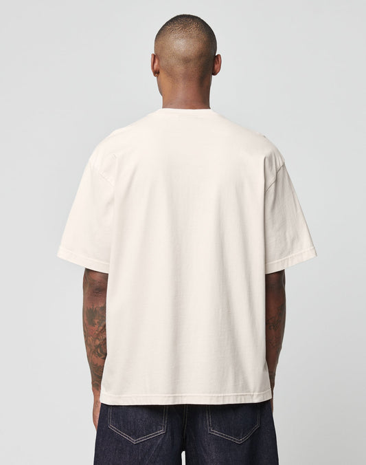 A person with short hair, seen from the back, is wearing the LIVE FAST DIE YOUNG Live Fast Ice Tee in beige and dark denim jeans against a light gray background.