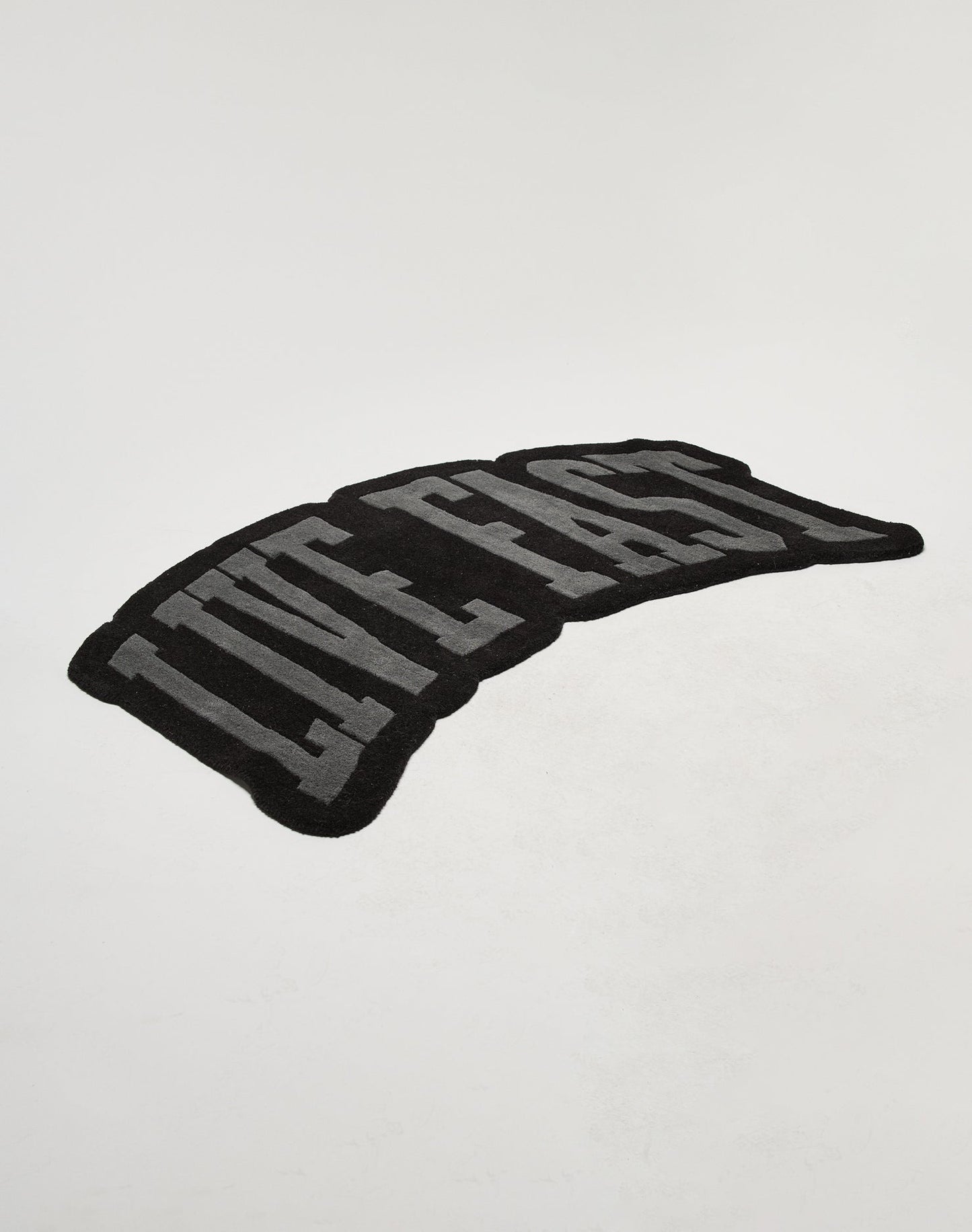 The Live Fast Carpet by LIVE FAST DIE YOUNG is a black rug featuring large gray LIVE FAST letters on a plain white background, made from 100% wool and easy to maintain with proper carpet care.