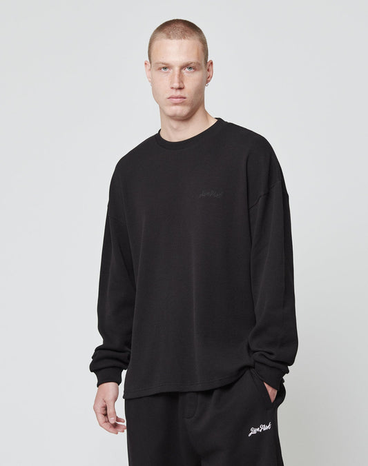 A person with short hair stands against a plain background, wearing an oversize fit Basic Script Waffle Longsleeve and matching black pants by LIVE FAST DIE YOUNG, both made from 100% Baumwolle, with subtle white text near the pocket.
