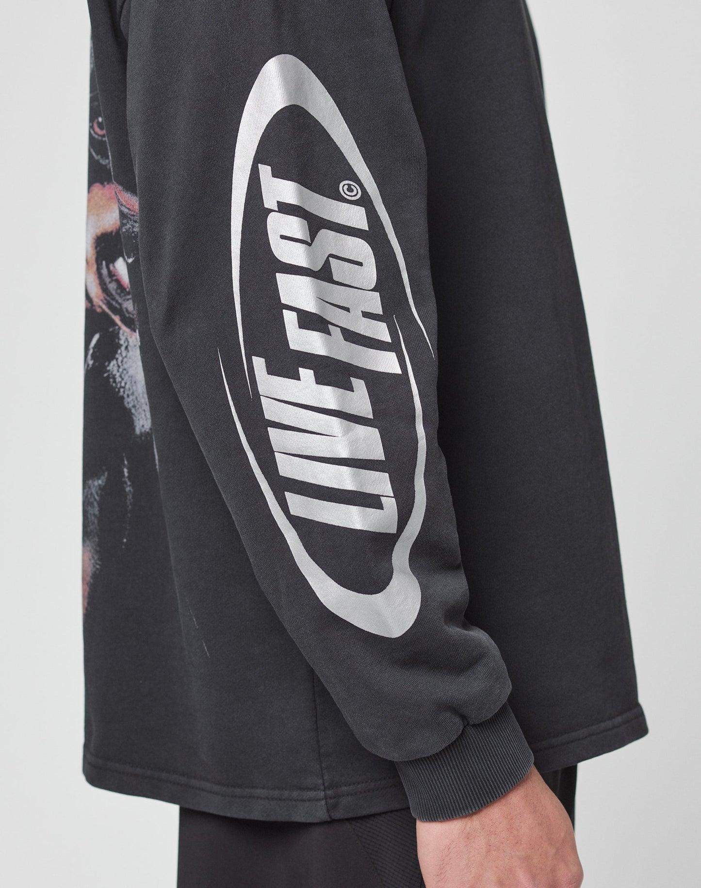 A person wears the LFDY Canine Longsleeve by LIVE FAST DIE YOUNG, an oversize black shirt with LIVE FAST in bold white letters and reflektierender Druck inside an oval on the sleeve, made from 100% Baumwolle.