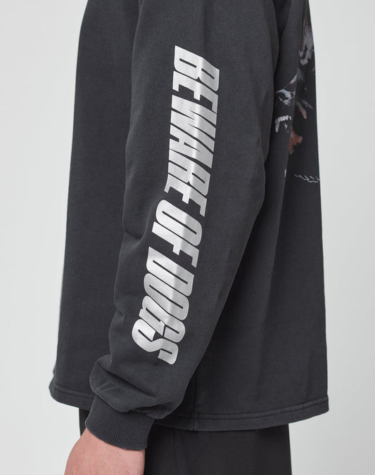A person wears the LFDY Canine Longsleeve by LIVE FAST DIE YOUNG, an oversized black shirt with BEWARE OF DOGS in bold reflective print down the sleeve. Only their arm and part of their torso are visible.