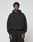 A young man with short, curly hair faces forward, wearing the LIVE FAST DIE YOUNG Basic 360 Hooded in black with front and back print and black pants against a plain light gray background.
