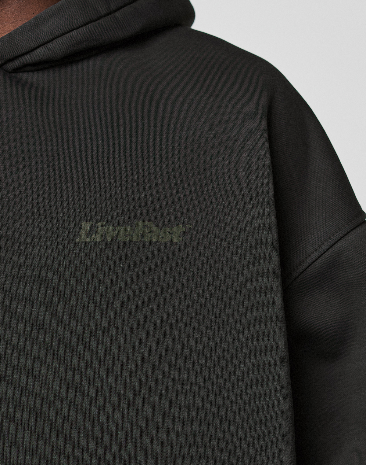 Close-up of the Basic 360 Hooded by LIVE FAST DIE YOUNG: an oversize fit black cotton sweatshirt with subtle "LiveFast" front print and additional print details on front and back. Soft, slightly textured fabric.