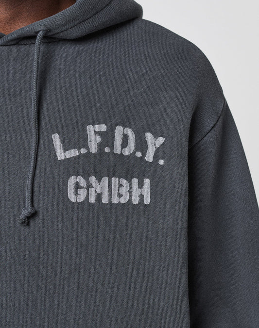 A close-up of the LFDY GmbH Hooded by LIVE FAST DIE YOUNG, a dark gray oversized hoodie with white "L.F.D.Y. above GMBH" text on the left chest and a visible drawstring on the left side of the hood.