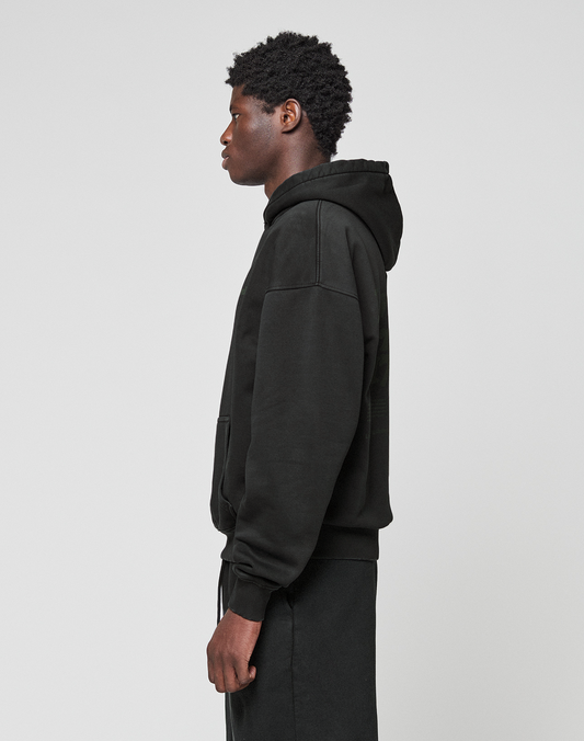 A person in profile wears the LIVE FAST DIE YOUNG Basic 360 Hooded in black and matching black pants against a plain light gray background. The hoodie features a subtle front and back print.