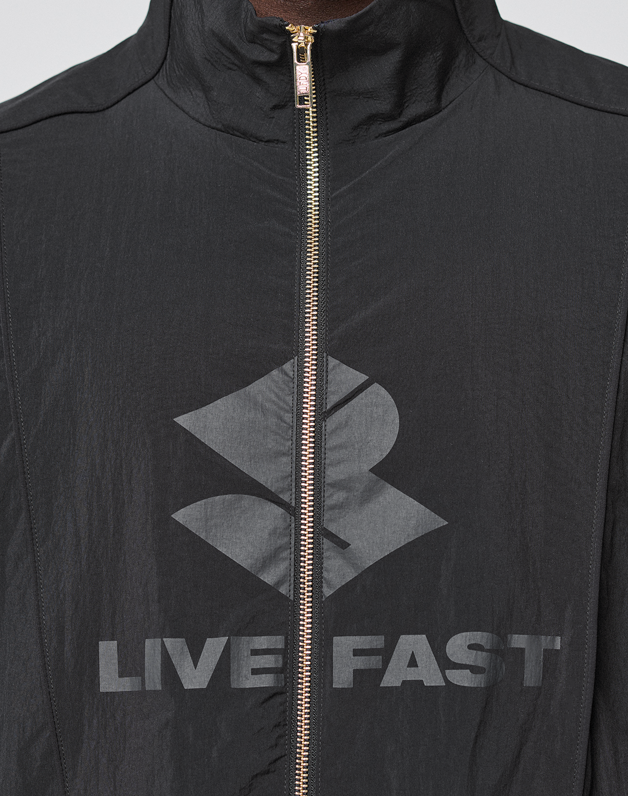 A close-up of the black LFDY Dealership Trackjacket by LIVE FAST DIE YOUNG, featuring a Regular Fit, silvery zipper, Stehkragen style, bold geometric logo, and gray "LIVE FAST" text across the chest.