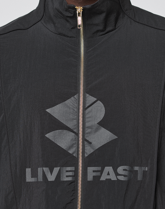A close-up of the black LFDY Dealership Trackjacket by LIVE FAST DIE YOUNG, featuring a Regular Fit, silvery zipper, Stehkragen style, bold geometric logo, and gray "LIVE FAST" text across the chest.