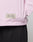 A close-up of a person in the LFDY Striped Padded Shirt by LIVE FAST DIE YOUNG, featuring pink and white vertical stripes and a "Live Fast" patch near the hem, paired with black pants; their right arm is bent at the elbow.