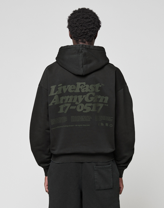 A person wearing the LIVE FAST DIE YOUNG Basic 360 Hooded black hoodie with the hood up, seen from behind. The back showcases large green "LiveFast ArmyGrn 17-0517" text and small writing—a stylish front and back print design. | model