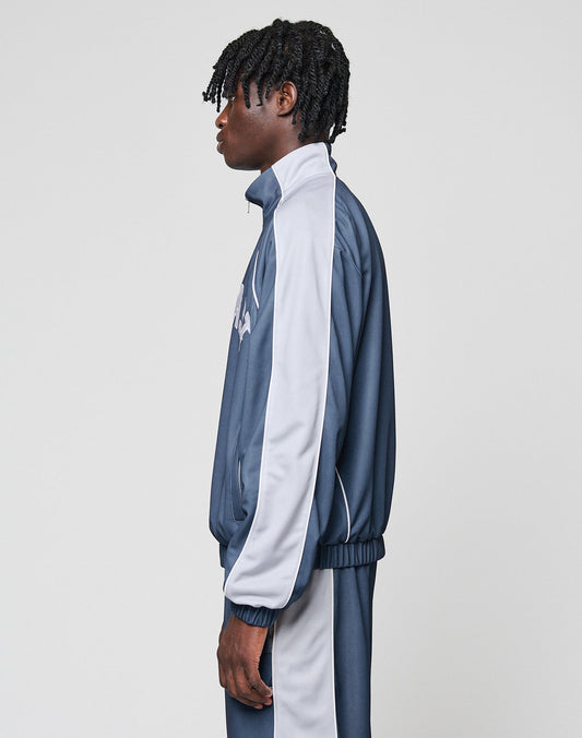 A person with short twisted hair stands in profile against a plain light background, wearing the oversized blue and light gray LFDY Arch Trackjacket by LIVE FAST DIE YOUNG with elastische Bündchen and matching pants.