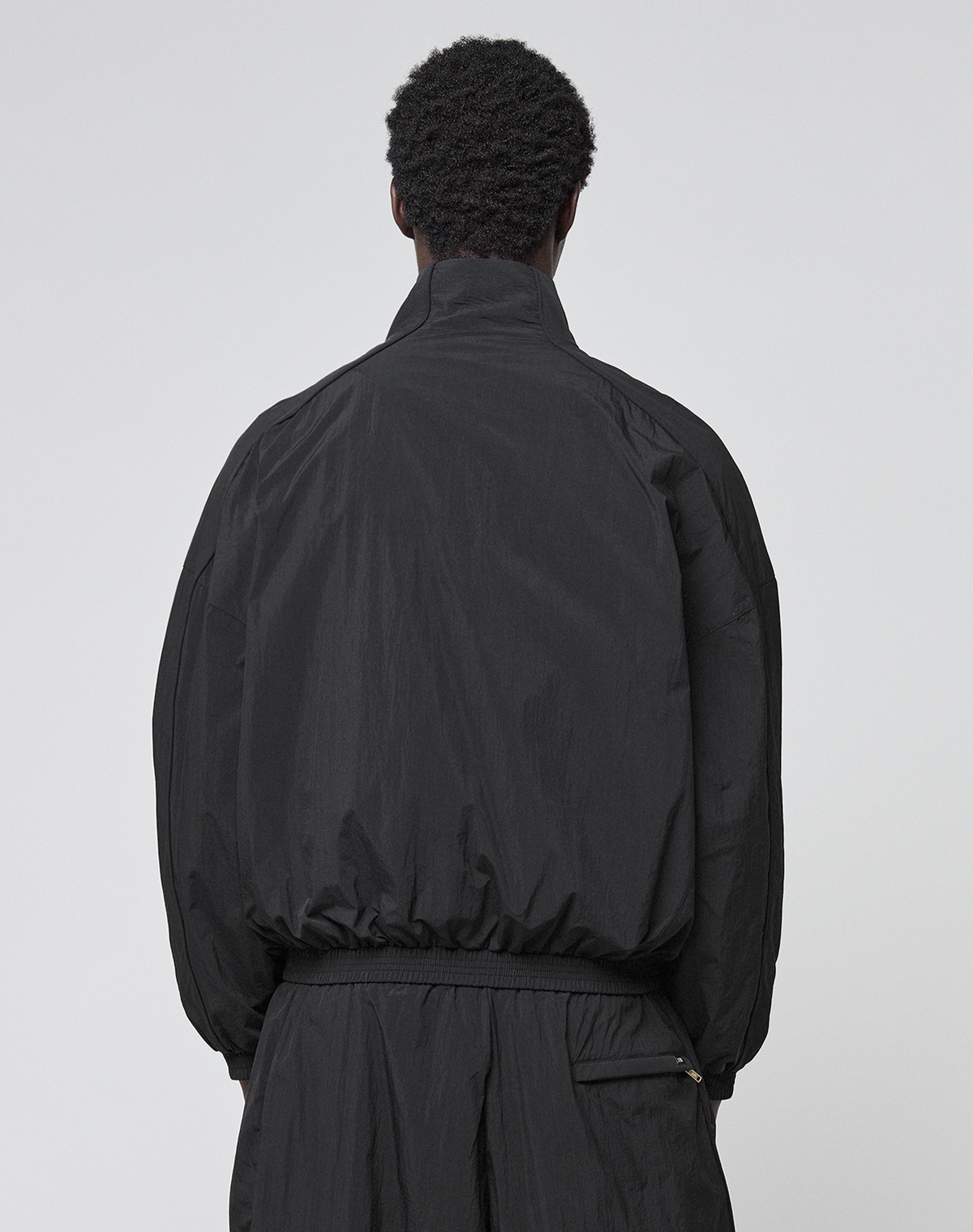 A person with short, curly hair stands with their back to the camera, wearing the black LIVE FAST DIE YOUNG LFDY Dealership Trackjacket and matching Regular Fit pants against a plain light gray background.