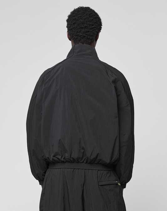 A person with short, curly hair stands with their back to the camera, wearing the black LIVE FAST DIE YOUNG LFDY Dealership Trackjacket and matching Regular Fit pants against a plain light gray background.