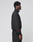 A person with short curly hair stands in profile against a plain background, wearing the LIVE FAST DIE YOUNG LFDY Dealership Trackjacket—black with a Stehkragen and a small red embroidered detail on the sleeve—paired with matching black pants.