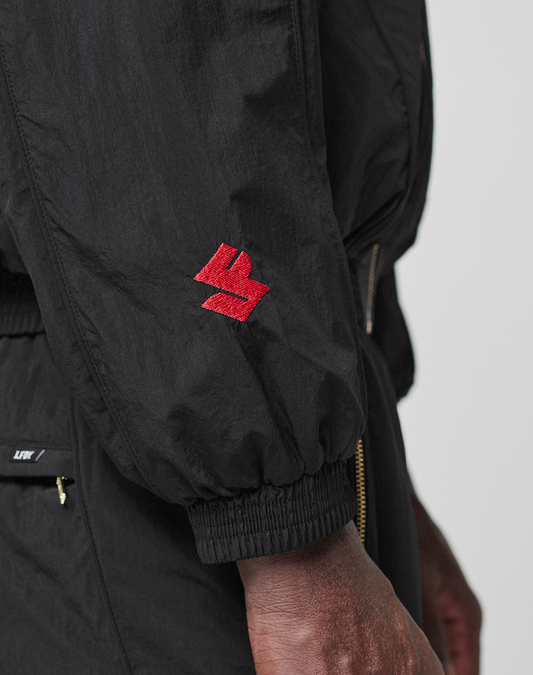 A close-up of a person's arm in the LFDY Dealership Trackjacket by LIVE FAST DIE YOUNG, featuring a red embroidered logo on the sleeve, elastic cuff, gold zippers, and a stylish Stehkragen.