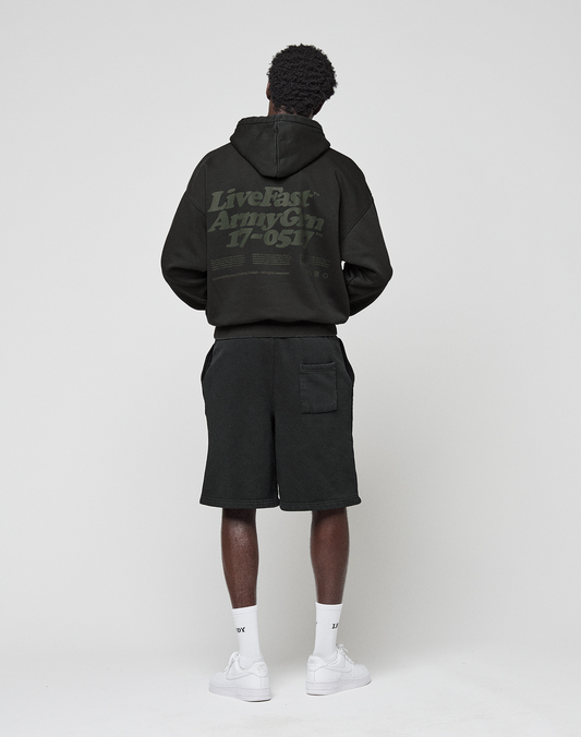 A person faces away, wearing the LIVE FAST DIE YOUNG Basic 360 Hooded black hoodie with "Live Fast Army Gn 17-051" back print, paired with black shorts, white socks, and white sneakers against a plain light background.