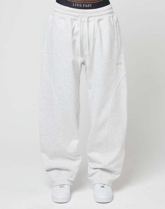 A person wears the LIVE FAST DIE YOUNG Basic Wide Jogger—loose, wide-fit light gray sweatpants with a visible black waistband featuring LIVE FAST text—paired with white sneakers, all set against a plain white background.