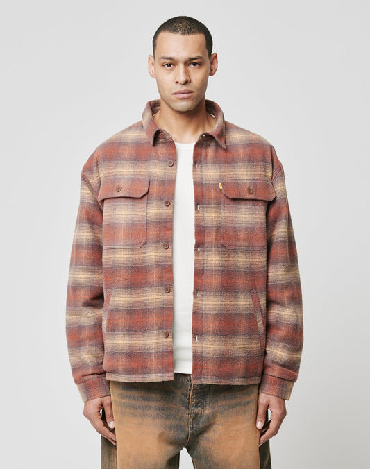 A man faces forward wearing the LIVE FAST DIE YOUNG Vintage Padded Flannel in red and beige plaid over a white shirt and brown pants, set against a plain light gray background. | model