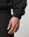 A close-up of a hand and wrist wearing the black Live Fast Nylon Jacket by LIVE FAST DIE YOUNG, featuring a textured finish, adjustable Velcro cuff strap, and side slit pockets. The background is plain and light-colored.