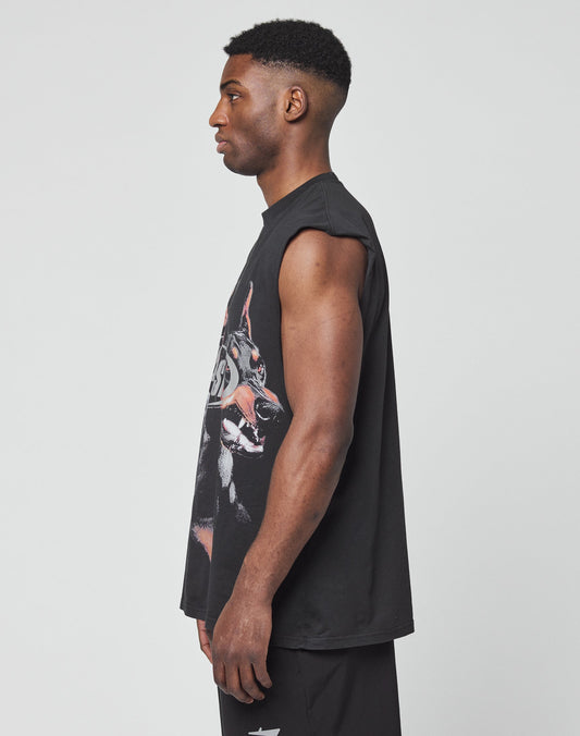 A man stands in profile against a white background, wearing the LIVE FAST DIE YOUNG LFDY Canine Muscle Shirt—a sleeveless black graphic T-shirt with silver print—and matching black shorts, his arms relaxed at his sides as he looks straight ahead.