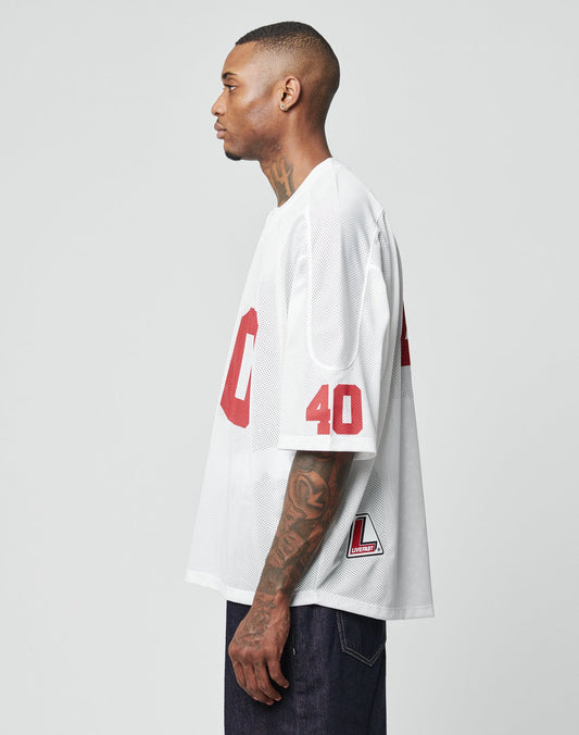 A man with neck and hand tattoos wears the LIVE FAST DIE YOUNG LFDY Mesh Jersey in white with red 40 on the sleeve, 00 on the front, oversize fit, V-neck, and pairs it with dark pants.