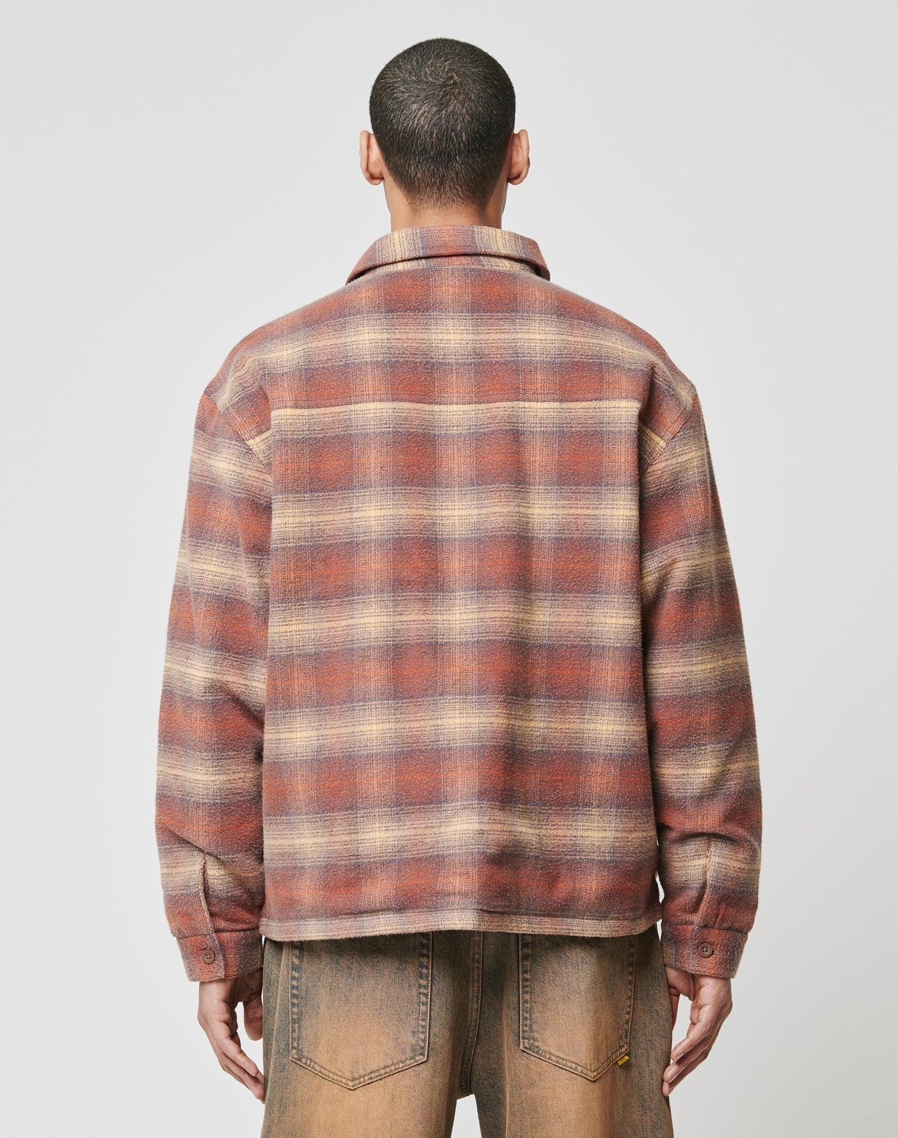 A person faces away from the camera, wearing LIVE FAST DIE YOUNGs Vintage Padded Flannel—an oversized brown and red plaid shirt—paired with faded brown pants, set against a plain light background.