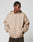 Wearing the LFDY Double Hooded Zip by LIVE FAST DIE YOUNG, a person stands with hands in pockets, looking down to the side. The beige zip-up has small LIVE FAST text on the chest, waffle lining, and is set against a plain light gray background.