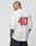 A man with short hair and tattoos wears the white LFDY Mesh Jersey by LIVE FAST DIE YOUNG, featuring a V-neck and red number 40 on the back. He faces away from the camera, glancing over his shoulder, paired with dark pants.