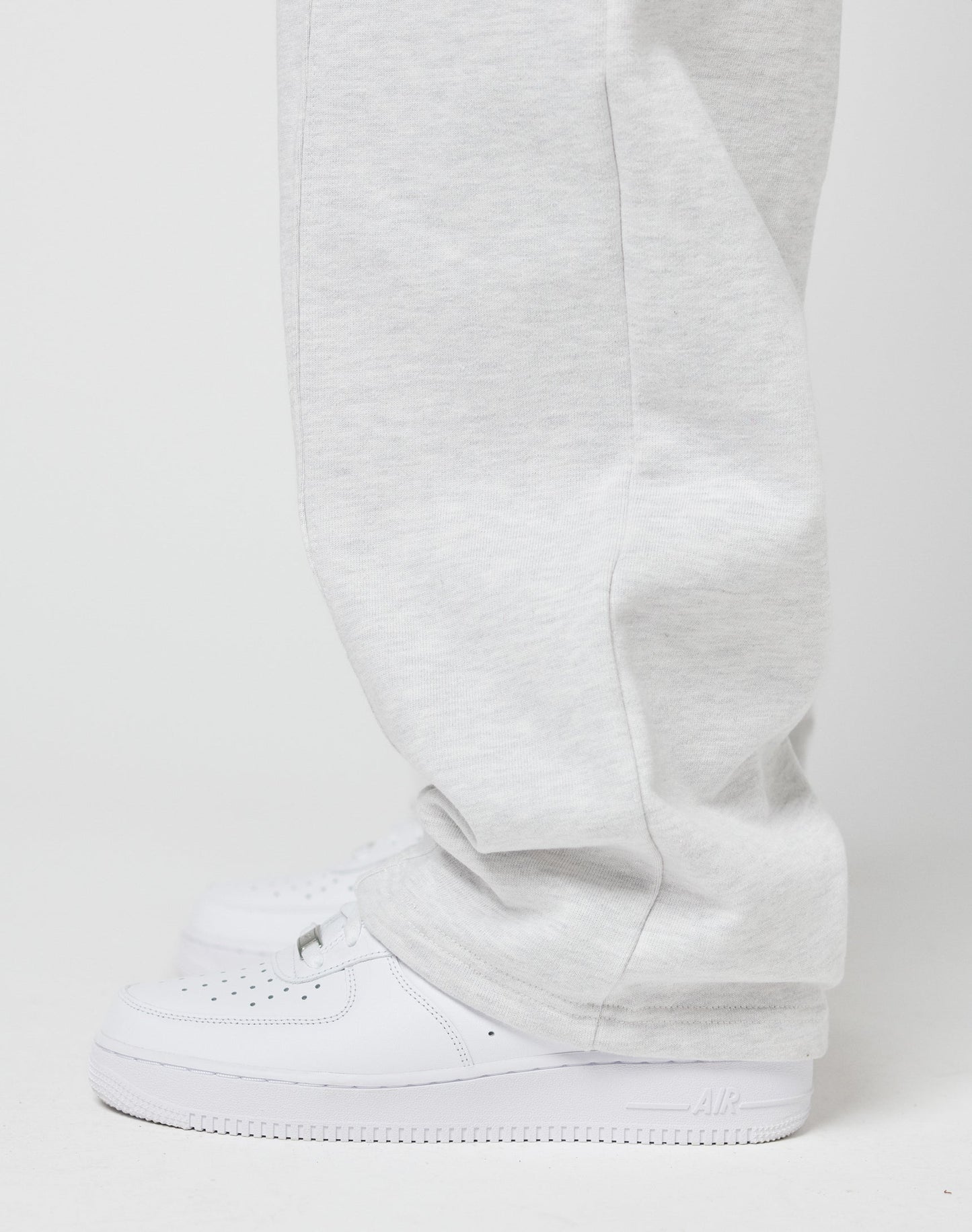 A person wearing LIVE FAST DIE YOUNG Basic Wide Jogger sweatpants in light gray and white Nike Air Force 1 sneakers stands against a plain white background.