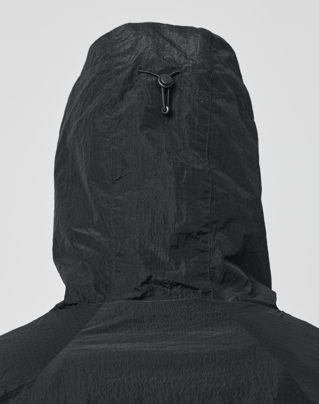 A close-up of the back of the LIVE FAST DIE YOUNG Live Fast Nylon Jacket, an oversized black hooded jacket with a cinch cord and toggle at the hood, shown against a plain light background.