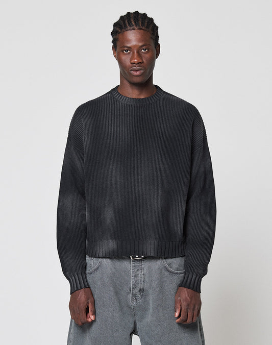 A person with braided hair wears the LIVE FAST DIE YOUNG LFDY Washed Knit Sweater, an oversized dark ribbed piece, paired with baggy gray 100% cotton jeans. They stand against a light gray background, facing forward with a neutral expression.