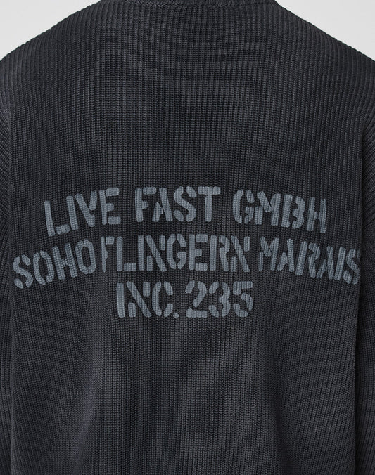 A close-up of the backprint on the black LFDY Washed Knit Sweater by LIVE FAST DIE YOUNG, featuring faded gray text and crafted from 100% Baumwolle for all-day comfort and style.