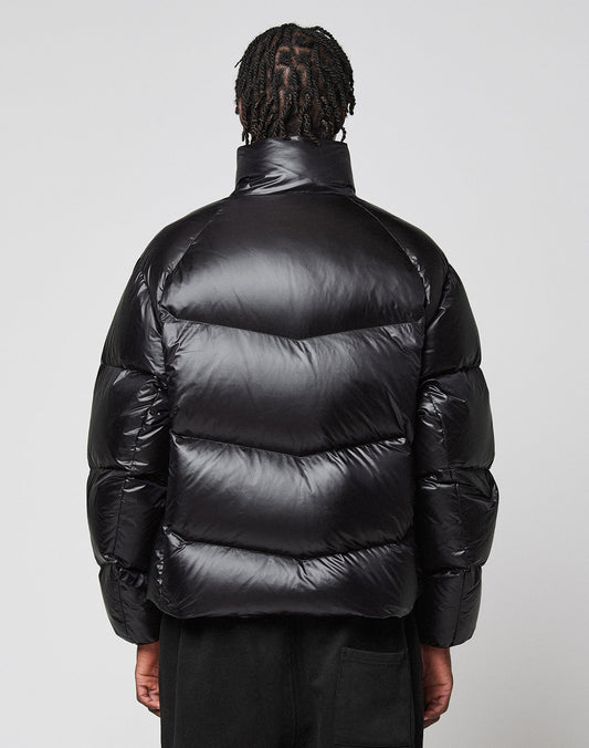 A person with short, twisted hair is seen from behind, wearing the Live Fast Down Jacket by LIVE FAST DIE YOUNG with 600er Fillpower and a shiny, wasserabweisend finish, against a plain light gray background.