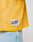 Close-up of a person wearing the LFDY Boxy Jersey by LIVE FAST DIE YOUNG—a yellow mesh top with boxy fit, paired with light blue jeans. The white tag reads LFDY OFFICIALLY LICENSED PRODUCT, size L in red.
