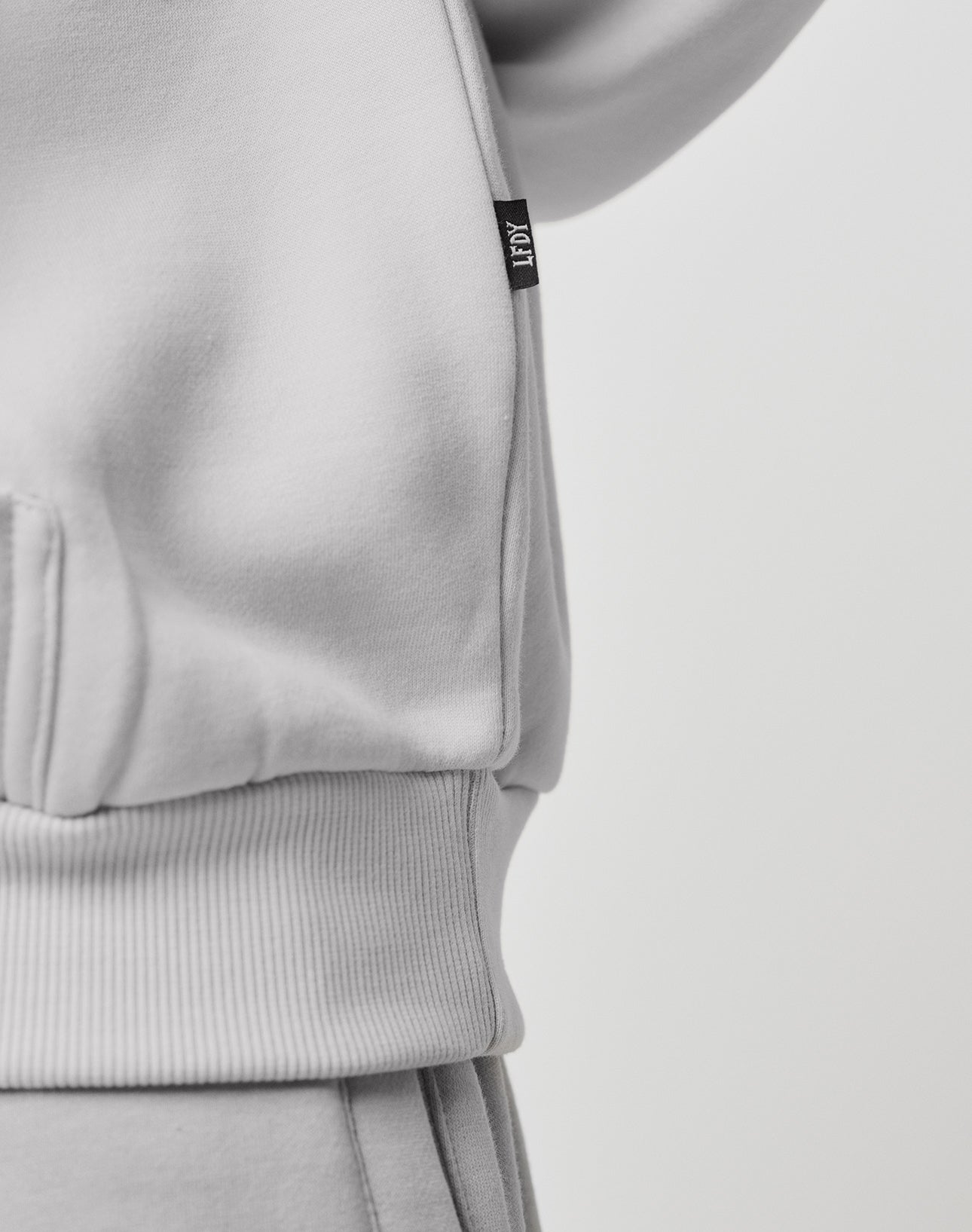 Close-up of the Basic Blank Hooded by LIVE FAST DIE YOUNG in light gray Oversize Fit, with ribbed waistband and a small black side tag. Made from a soft cotton-polyester blend for comfort.