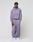 A young man wears the LIVE FAST DIE YOUNG LFDY Hotline Loose Jogger with Elastikbund and Print am Bein, paired with a lavender hoodie and white sneakers, standing against a plain background and looking at the camera neutrally.