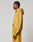 A person stands in profile wearing the LIVE FAST DIE YOUNG Live Fast Sweatsuit Jacket, an oversized mustard yellow hoodie with matching sweatpants featuring red front print text and graphics, against a plain light-colored background.