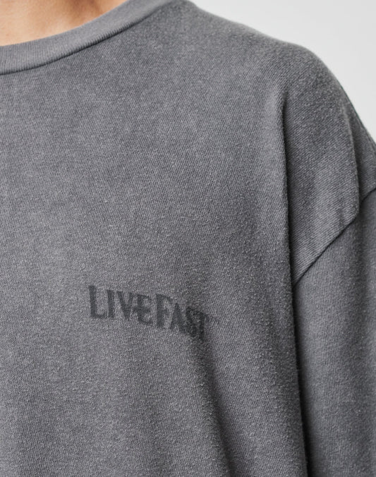 A close-up of a person wearing the LFDY Loyal Tee by LIVE FAST DIE YOUNG, an oversize fit gray T-shirt featuring LIVE FAST in black on the left chest, accentuating the shoulder and upper chest area.