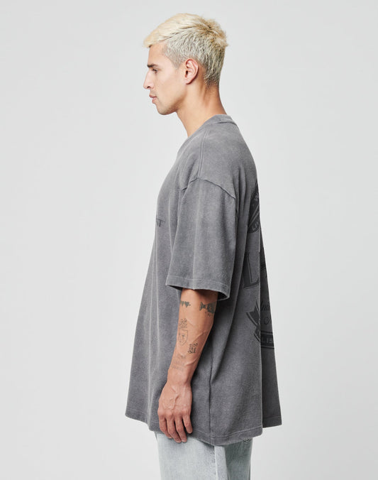 A young man with short, bleached blond hair stands in profile against a light background, wearing the LIVE FAST DIE YOUNG LFDY Loyal Tee in faded gray and light jeans. Tattoos are visible on his left arm.