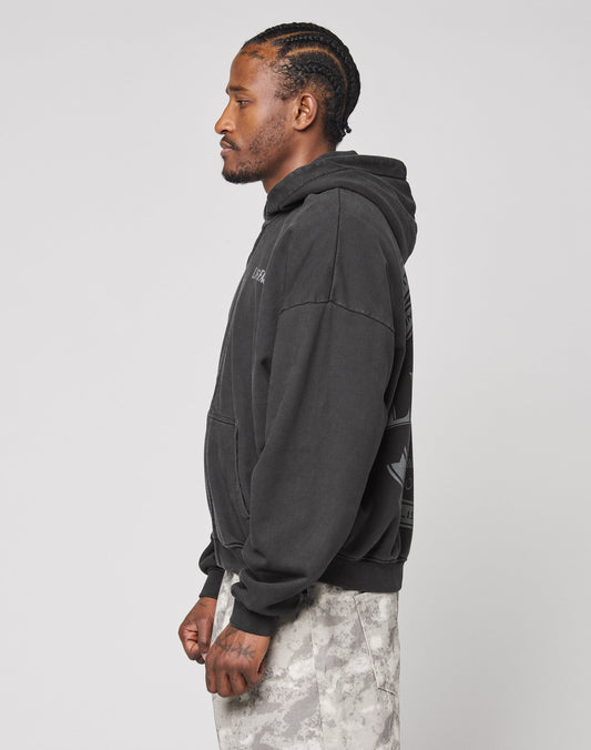 A man with braided hair stands in profile, wearing a black LFDY Loyal Hooded Zip by LIVE FAST DIE YOUNG and light camouflage pants against a plain light background.