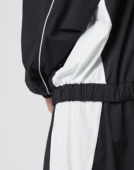 A close-up of a person in the LIVE FAST DIE YOUNG Basic Nylon Trackjacket and regular fit pants with seitliche Eingrifftaschen, elastic waistband, and loose sleeves, standing against a plain light background.