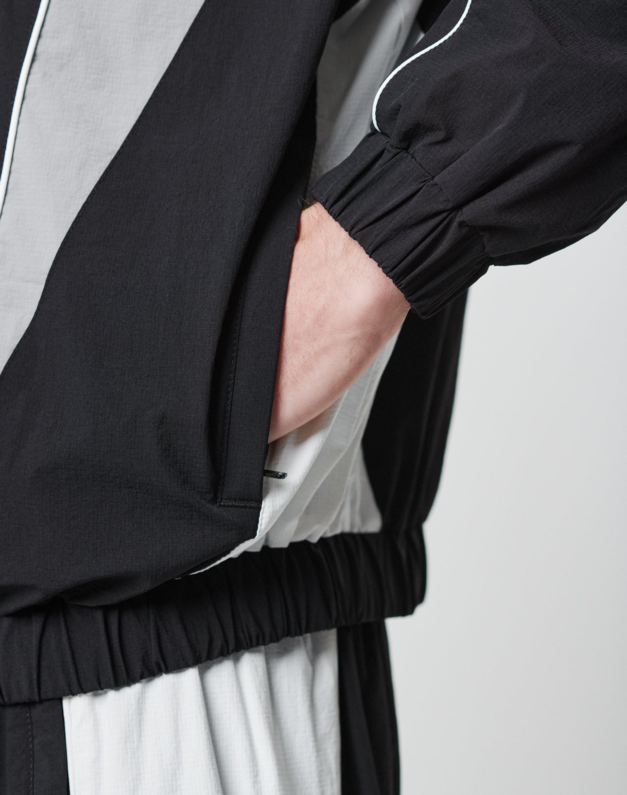 A person wearing the LIVE FAST DIE YOUNG Basic Nylon Trackjacket in black and white, with one hand in their pocket, shown from waist to just below the shoulder.