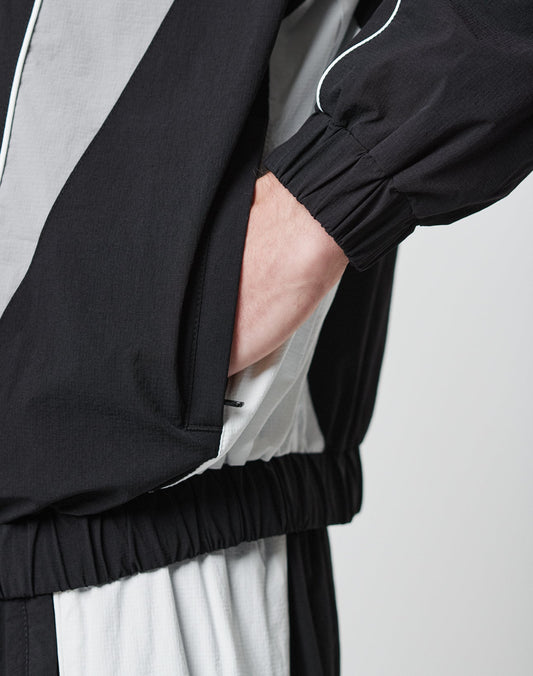 A person wearing the LIVE FAST DIE YOUNG Basic Nylon Trackjacket in black and white, with one hand in their pocket, shown from waist to just below the shoulder.