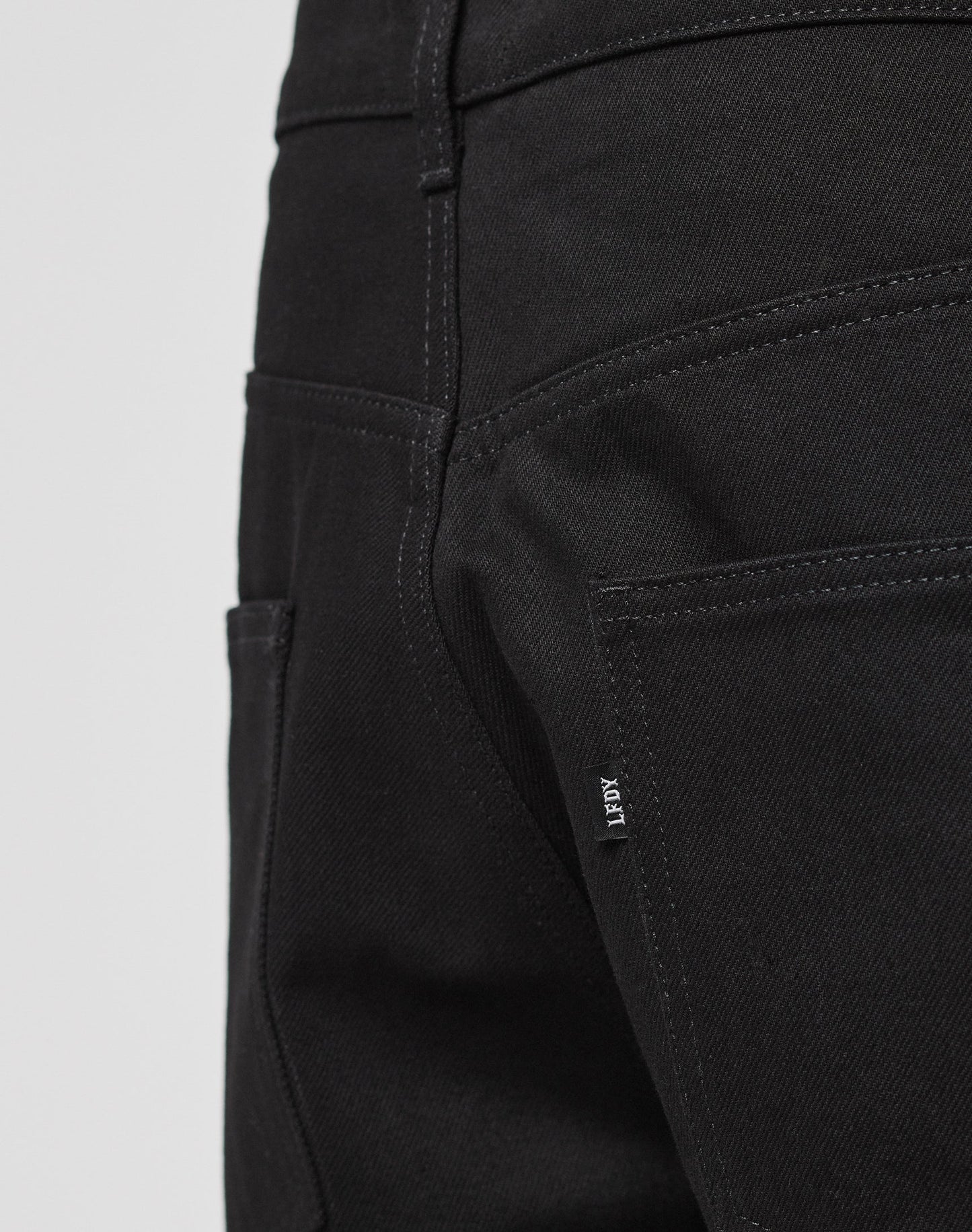 Close-up of the back pocket area of LFDY Baggy Denim in black, featuring visible stitching and a small fabric tag on the seam. Made from 100% Baumwolle for lasting comfort and durability.