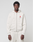 A person in a light beige LFDY Heavyweight Lounge Zip Hooded by LIVE FAST DIE YOUNG and matching sweatpants faces forward. The regular fit hoodie has a small red logo and “LIVEFAST” text on the left chest. Background is plain and light-colored.