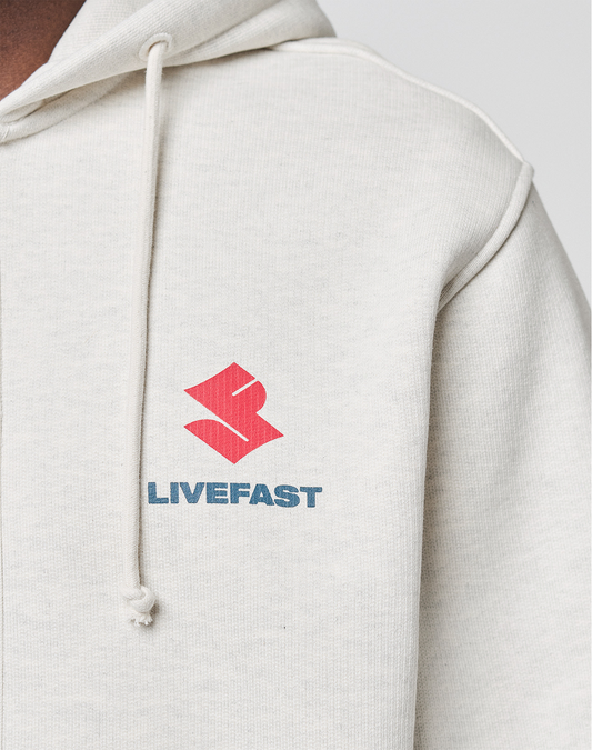 Close-up of the LFDY Heavyweight Lounge Zip Hooded by LIVE FAST DIE YOUNG in light beige, featuring a red abstract logo and blue LIVEFAST text on the left chest. Made from 100% Baumwolle with drawstrings and a comfortable Regular Fit.