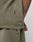 A close-up shows a person wearing the LIVE FAST DIE YOUNG Basic +49 Tee in olive green Oversize Fit, with part of their shirt and pants visible. A small black tag is on the shirt, and a tattoo can be seen on their right arm.