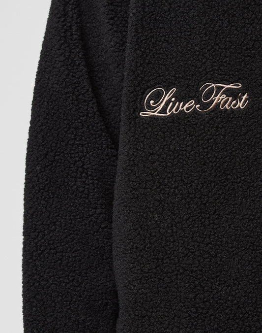 Close-up of the LFDY Teddy Jacket by LIVE FAST DIE YOUNG, featuring black textured fleece, raglan sleeves, and "Live Fast" embroidered in cursive with light-colored thread.