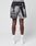 A person stands facing away, showing only their lower half, wearing LIVE FAST DIE YOUNG LFDY Performance Shorts with a blurry black and white print, paired with white socks and white sneakers featuring a reflective logo print, against a plain light background.