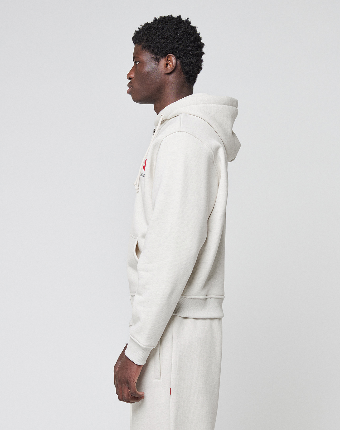 A person in profile wears the LIVE FAST DIE YOUNG LFDY Heavyweight Lounge Zip Hooded in light beige with matching sweatpants, standing against a plain light background.